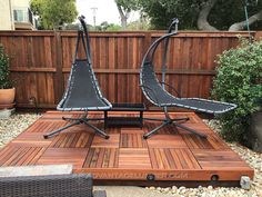 two lawn chairs sitting on top of a wooden deck in front of a garden fence