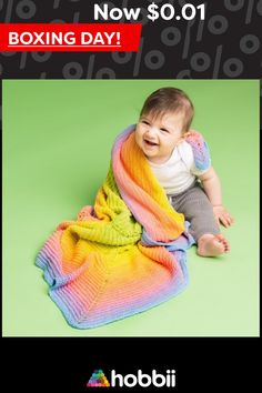 a baby sitting on the ground with a rainbow blanket over it's head and smiling