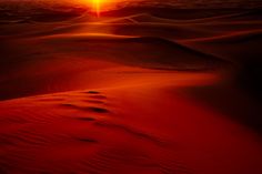 the sun is setting in the desert with sand dunes and red water ripples around it