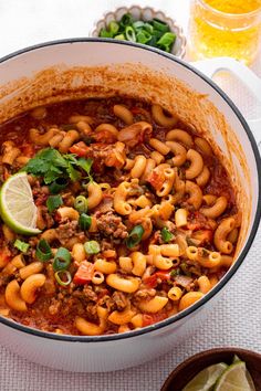 a large pot filled with pasta and meat on top of a table next to limes