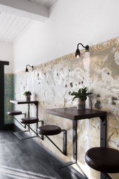 three tables and two stools in front of a wall with peeling paint on it