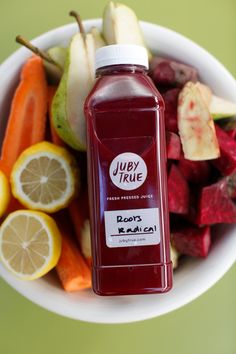 a white bowl filled with lots of fruit and veggies next to a bottle of juice