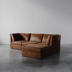 a brown leather sectional sofa sitting on top of a cement floor next to a white wall