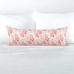 an orange and white flowered pillow sitting on top of a bed next to pillows