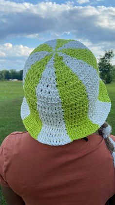 a person wearing a green and white crocheted hat in the grass with trees in the background