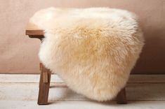 a white sheepskin stool sitting on top of a wooden floor next to a wall