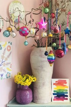 a vase with ornaments hanging from it on a shelf next to a painting and flowers