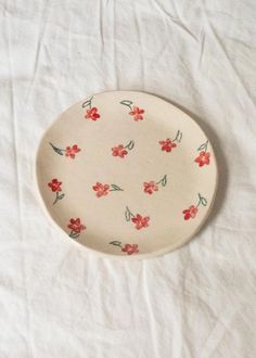 a white plate with red flowers and green leaves on it sitting on a white sheet