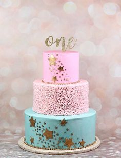 a three tiered cake with stars on top and one number on the top is pink, blue, and gold