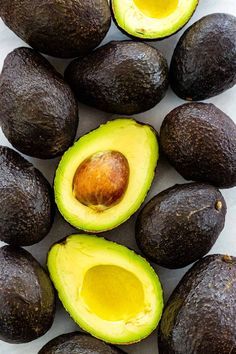 an avocado cut in half on a white surface with other fruits around it