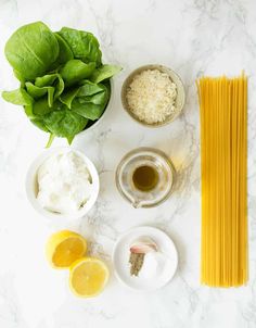 ingredients to make pasta laid out on a marble counter top with basil, lemons, garlic and parmesan cheese