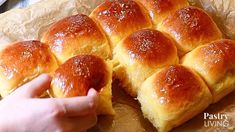 a person reaching for some bread rolls on a piece of wax paper with the buns cut in half