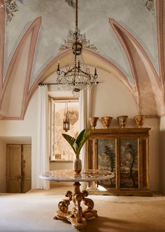 a room with a chandelier hanging from the ceiling and a table in front of it