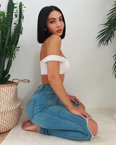 a woman sitting on the floor next to a potted plant and wearing blue jeans