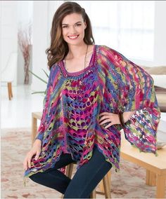 a woman is smiling while sitting on a bench wearing a colorful knitted ponchy