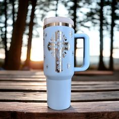 a white and blue cup sitting on top of a wooden table next to some trees