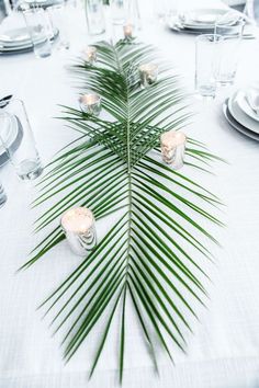 there is a palm leaf on the table with place settings and silverware around it