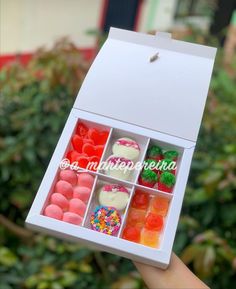 a hand holding a box filled with lots of different types of candies in it