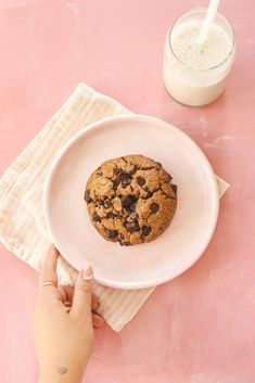 a person holding a plate with a chocolate chip cookie on it next to a glass of milk