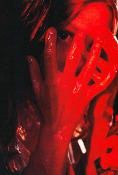 a woman covering her face with hands and looking at the camera while she is covered in red paint