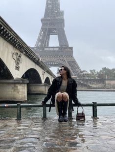 a woman sitting on a rail in front of the eiffel tower