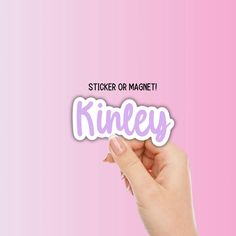 a hand holding up a sticker that says sticker or magnet kinley