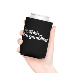 a hand holding a black can cooler with the words shh i'm gambling printed on it