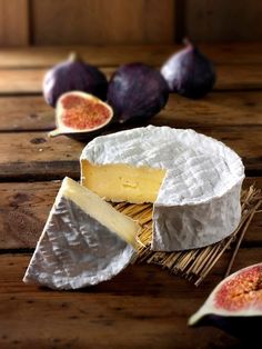 some cheese is sitting on a table next to figs and other food items that are cut in half