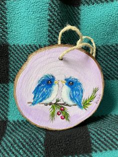 two blue birds sitting on top of a piece of wood with green leaves and berries