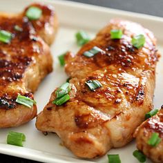 three pieces of meat on a plate with green onions