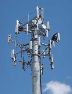 a tall metal pole with many antennas on it's sides and a bird perched on top