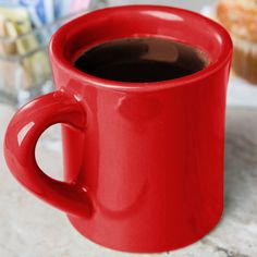 a red coffee cup sitting on top of a counter next to a muffins