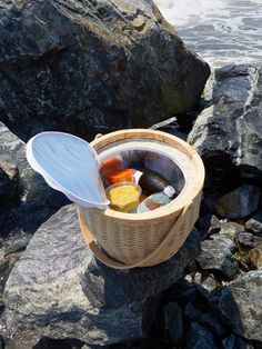 a basket filled with bottles sitting on top of a rock next to the ocean and water