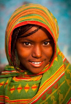 a woman with braids in a green and yellow shawl smiles at the camera