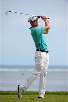 a man swinging a golf club on top of a grass covered field next to the ocean