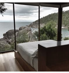 there is a bed in the room with large windows looking out at the water and mountains