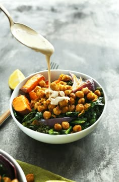 a person pouring dressing into a bowl filled with vegetables and chickpeas on a table