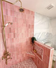 a pink tiled bathroom with gold fixtures and shower head in the corner on the wall