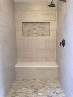 a walk in shower sitting next to a white tiled wall and floor with a black faucet