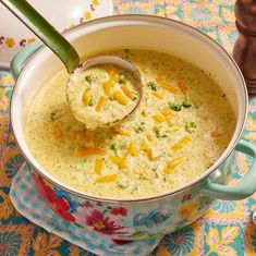 a ladle full of broccoli cheese soup on a colorful place mat with spoon