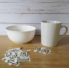 a cup and some stickers sitting on a table next to a bowl with the word drink written in it