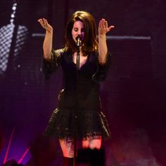 a woman standing on top of a stage holding her hands up in the air while singing into a microphone