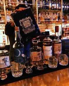 a bar with bottles and glasses sitting on it's counter, in front of a man holding up a sign