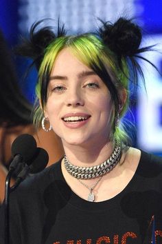 a woman with green and yellow hair smiles at the camera while speaking into a microphone