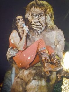 a woman sitting on top of a giant monster next to a man in red pants