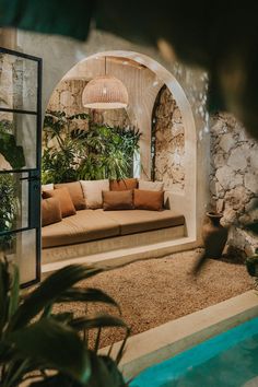 an outdoor living area with couches, potted plants and a stone wall in the background