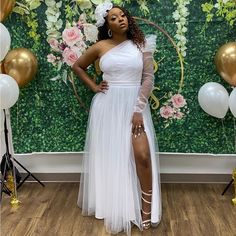 a woman standing in front of a floral backdrop wearing a white dress with sheer sleeves