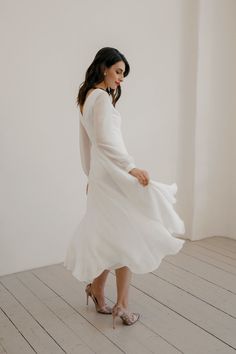 a woman in a white dress is standing on a wooden floor and looking down at her shoes