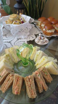 sandwiches and pastries are arranged on a glass platter with lace doily around them