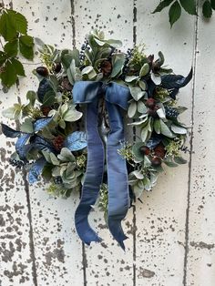 a wreath hanging on the side of a white wooden wall with blue ribbon and green leaves